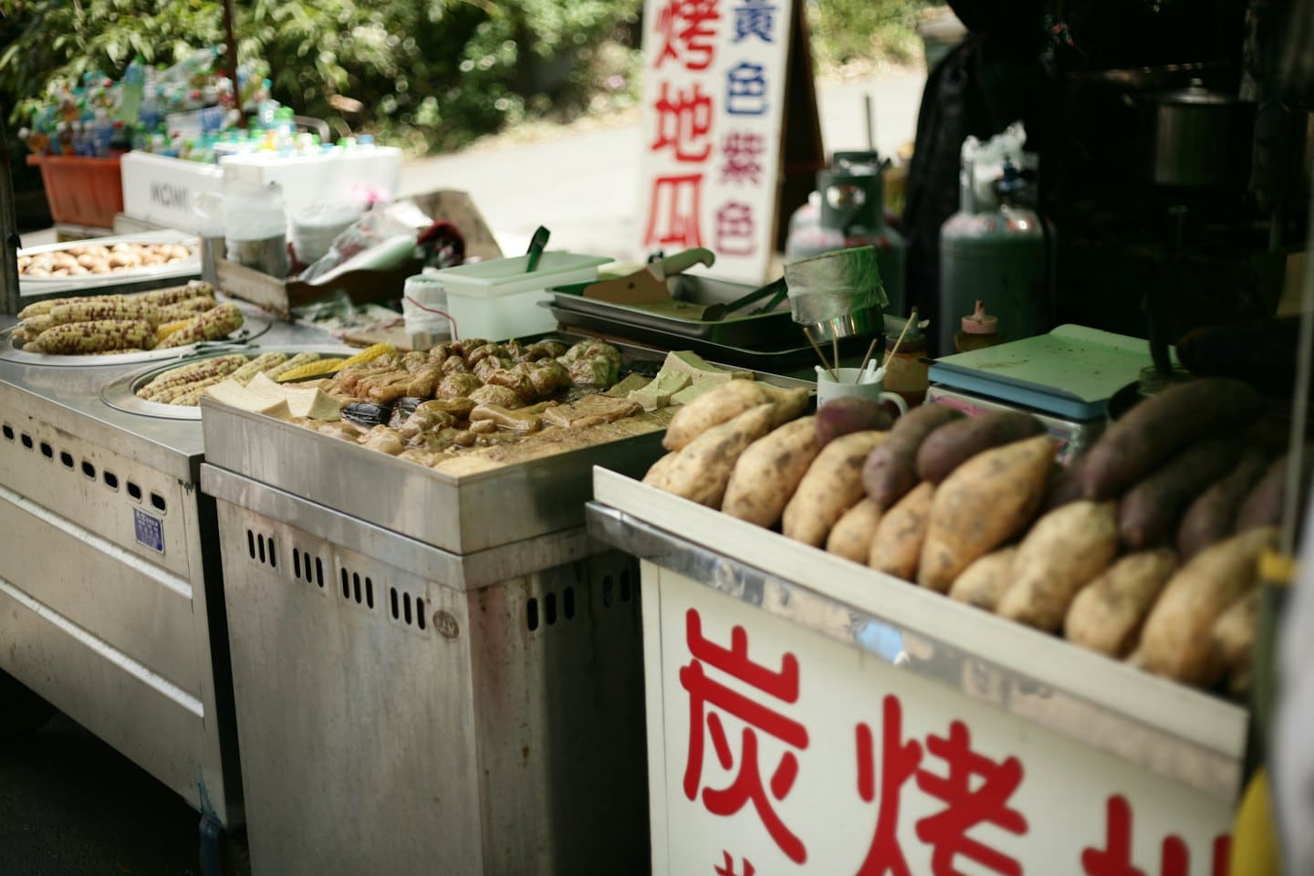 Street food stall displaying warm cooked dishes and raw sweet potatoes.