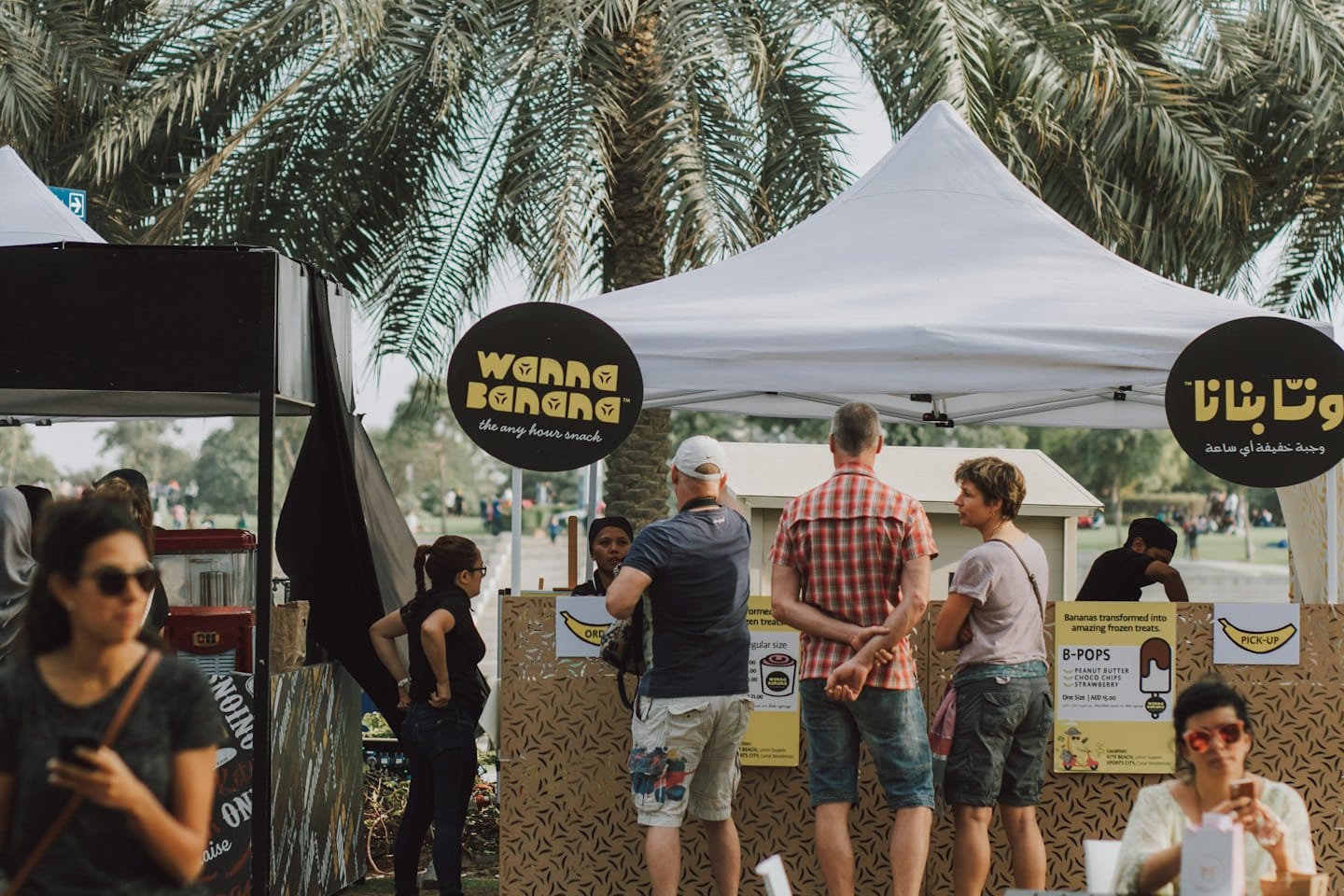 Diverse customers buy food from a stall at an outdoor market.