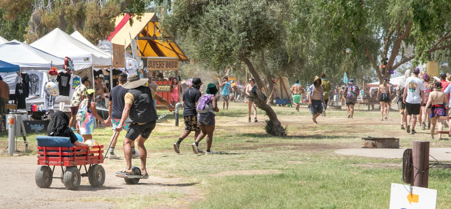 People enjoying a sunny outdoor festival with vendor stalls and a unicycle.