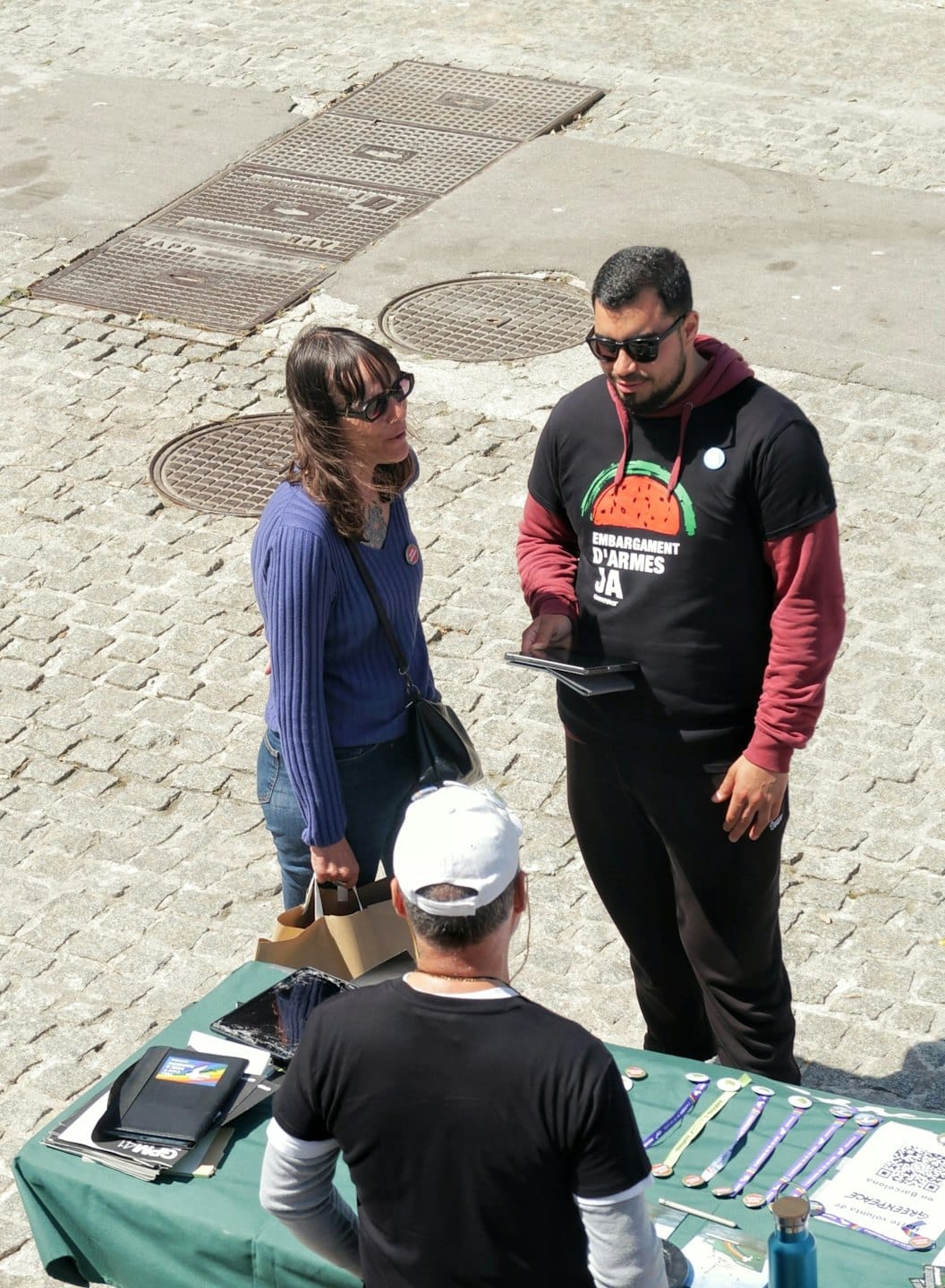 Two customers converse with a street vendor at an outdoor booth.